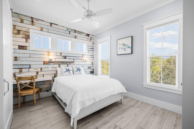 bedroom with baseboards, ceiling fan, ornamental molding, wood walls, and light wood-style floors