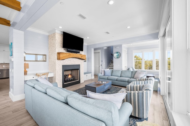 living area featuring a fireplace, light wood finished floors, visible vents, stairway, and ornamental molding