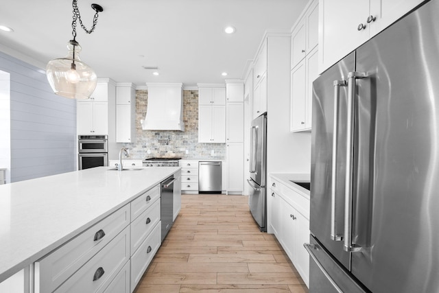 kitchen featuring light wood finished floors, tasteful backsplash, custom exhaust hood, stainless steel appliances, and light countertops