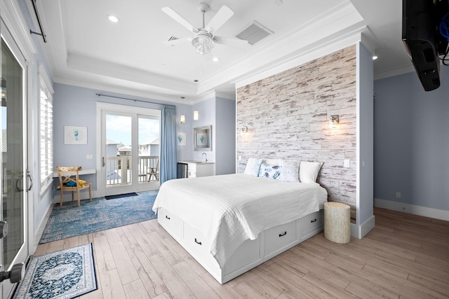 bedroom with a raised ceiling, an accent wall, access to exterior, crown molding, and light wood-type flooring