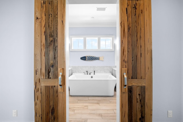 bathroom with ornamental molding, wood tiled floor, and a freestanding bath