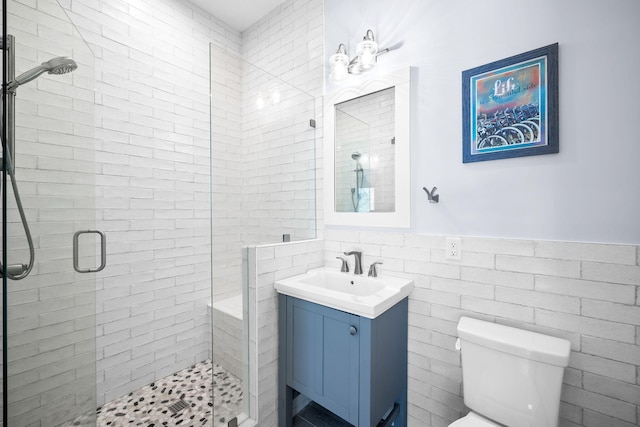 bathroom with a wainscoted wall, tile walls, toilet, a stall shower, and vanity