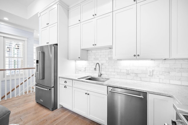 kitchen with stainless steel appliances, a sink, white cabinets, light wood-style floors, and backsplash