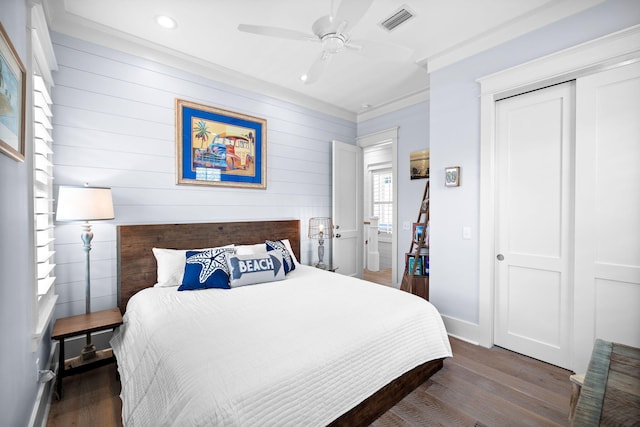 bedroom featuring wood finished floors, visible vents, baseboards, ornamental molding, and a closet