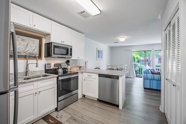 kitchen featuring stainless steel appliances, visible vents, light wood-style floors, a sink, and a peninsula