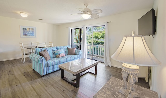 living area featuring a ceiling fan, visible vents, baseboards, and wood finished floors