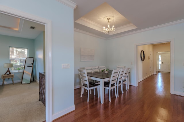 dining space with a notable chandelier, a raised ceiling, visible vents, ornamental molding, and wood finished floors