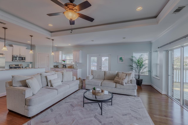 living area with baseboards, visible vents, ornamental molding, wood finished floors, and a tray ceiling