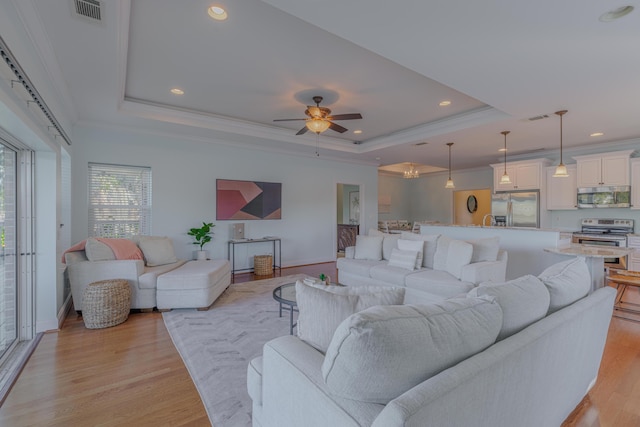 living area featuring light wood-type flooring, visible vents, a tray ceiling, and ornamental molding