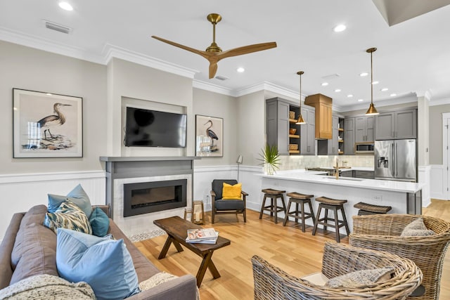 living area featuring a wainscoted wall, a fireplace, crown molding, visible vents, and light wood-style floors