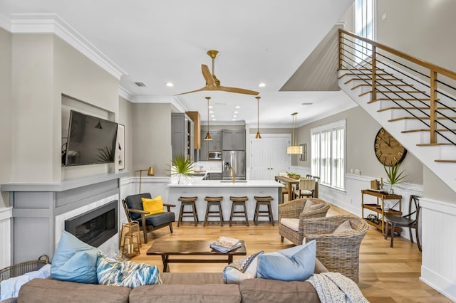 living area featuring visible vents, a glass covered fireplace, a wainscoted wall, crown molding, and light wood-style floors