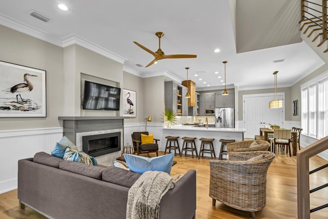 living room featuring ornamental molding, a glass covered fireplace, wainscoting, and visible vents