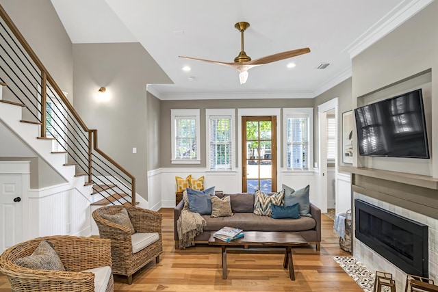 living area featuring ornamental molding, stairway, a tiled fireplace, and wood finished floors