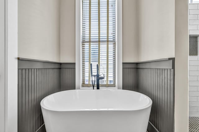 bathroom featuring a soaking tub, wainscoting, and a sink