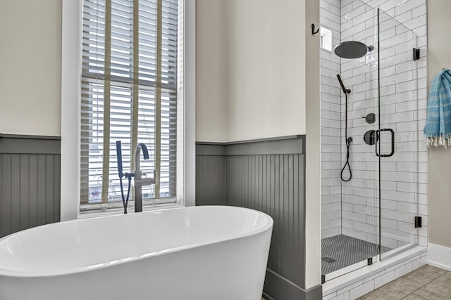 bathroom with a soaking tub, a shower stall, a sink, and a wainscoted wall