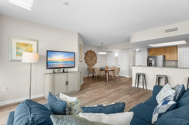 living area with light wood-style flooring, visible vents, and baseboards