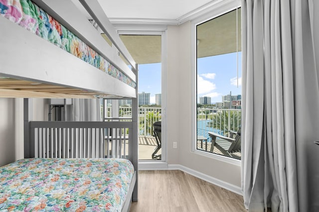 bedroom featuring access to exterior, a city view, baseboards, and wood finished floors