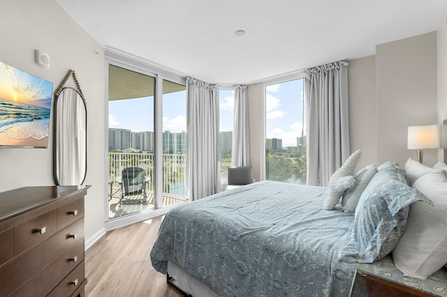 bedroom with light wood-style floors, access to outside, a wall of windows, and a city view