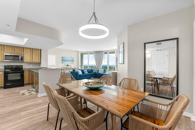 dining space with light wood-type flooring, a skylight, visible vents, and baseboards