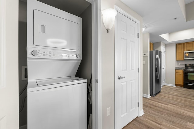 laundry area with light wood finished floors, laundry area, baseboards, and stacked washer / dryer