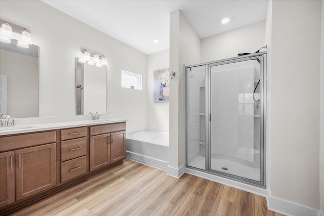 bathroom with a stall shower, a sink, a bath, and wood finished floors