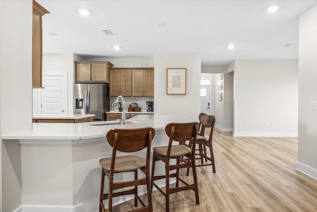 kitchen with a sink, a breakfast bar, light wood-type flooring, and stainless steel fridge