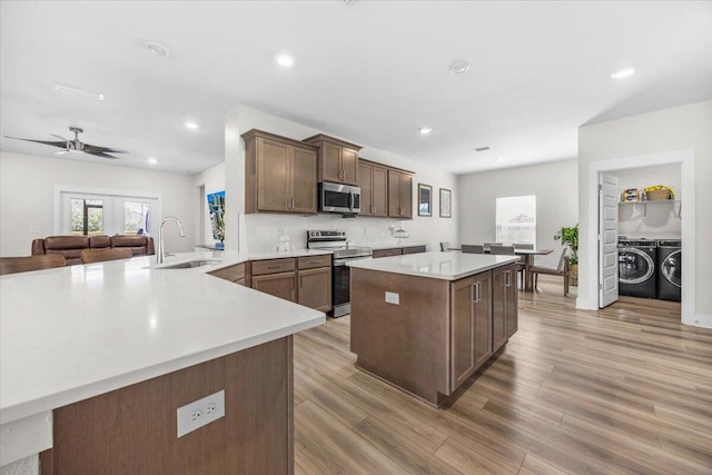 kitchen featuring stainless steel appliances, light countertops, light wood-style flooring, a sink, and separate washer and dryer