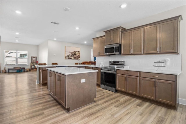 kitchen with a peninsula, light wood-style floors, tasteful backsplash, and appliances with stainless steel finishes