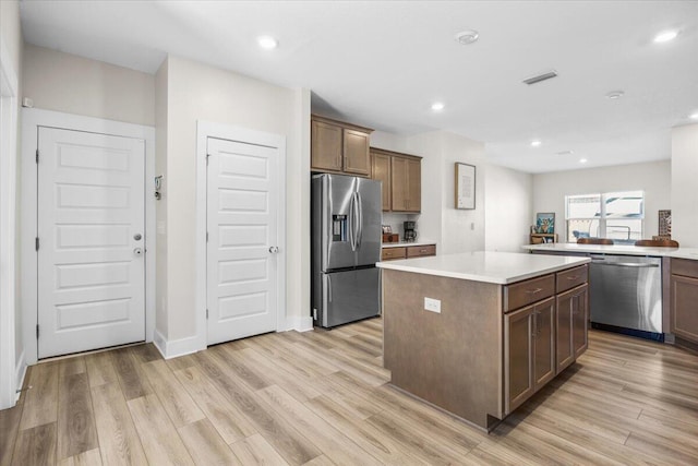 kitchen with stainless steel appliances, visible vents, light wood-style floors, light countertops, and a center island