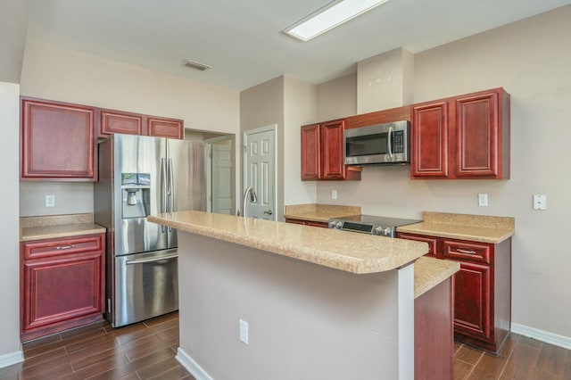 kitchen featuring a kitchen island with sink, light countertops, appliances with stainless steel finishes, wood tiled floor, and reddish brown cabinets