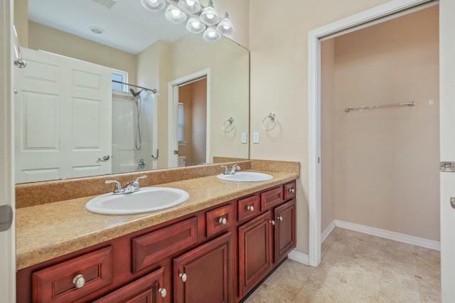 full bath featuring walk in shower, a sink, baseboards, and double vanity