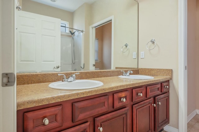 bathroom featuring double vanity, walk in shower, a sink, and baseboards