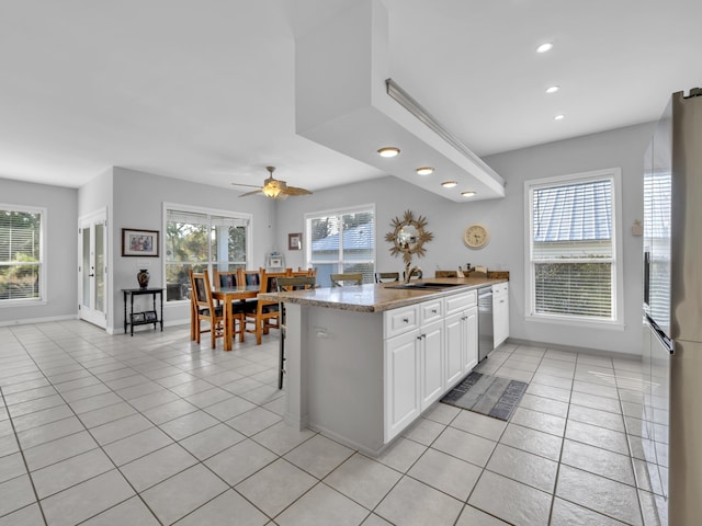 kitchen with light tile patterned floors, a peninsula, stainless steel appliances, white cabinetry, and a wealth of natural light