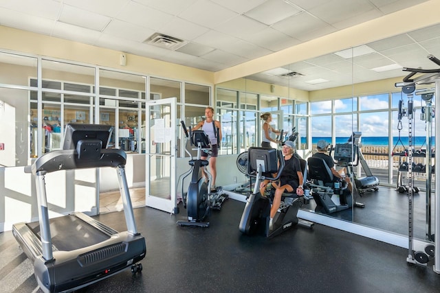 exercise room with a paneled ceiling, visible vents, and a water view