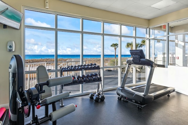 exercise room featuring a paneled ceiling, a water view, and a beach view