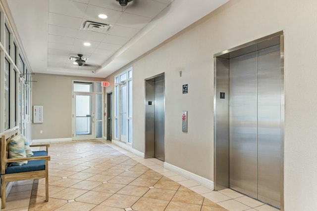 hall with light tile patterned floors, a raised ceiling, visible vents, and elevator