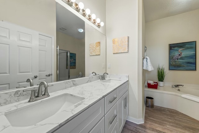 bathroom with double vanity, wood finished floors, a sink, and a bath