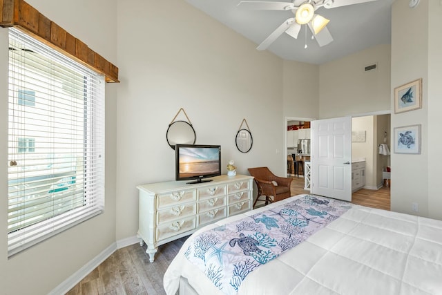 bedroom with stainless steel refrigerator with ice dispenser, visible vents, a towering ceiling, wood finished floors, and baseboards