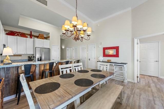 dining space with visible vents, baseboards, ornamental molding, light wood finished floors, and an inviting chandelier