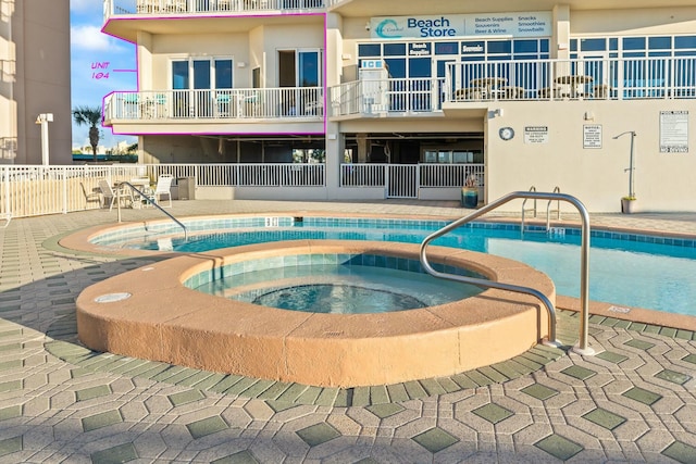 community pool with a patio area, fence, and a hot tub