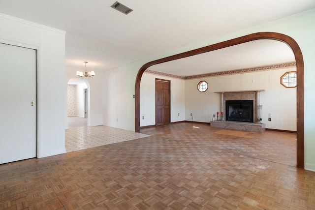 unfurnished living room with visible vents, a fireplace with raised hearth, arched walkways, a textured ceiling, and a chandelier