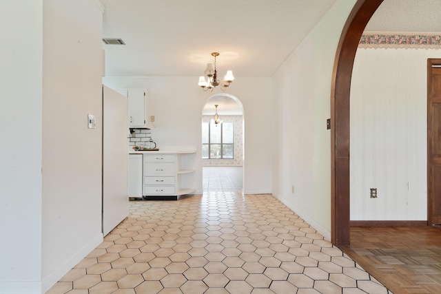 interior space with an inviting chandelier, visible vents, arched walkways, and baseboards