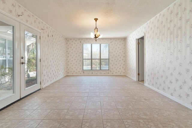 spare room with french doors, baseboards, a textured ceiling, and wallpapered walls