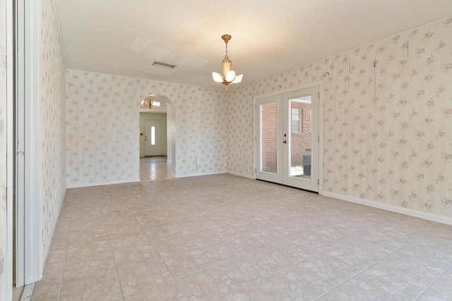 empty room featuring wallpapered walls, a notable chandelier, baseboards, and arched walkways