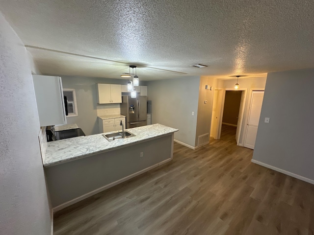 kitchen featuring a peninsula, a sink, visible vents, dark wood-style floors, and stainless steel fridge