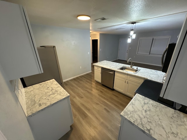 kitchen featuring a peninsula, wood finished floors, a sink, visible vents, and stainless steel dishwasher