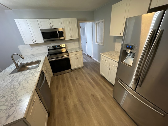 kitchen with appliances with stainless steel finishes, a sink, light wood finished floors, and decorative backsplash