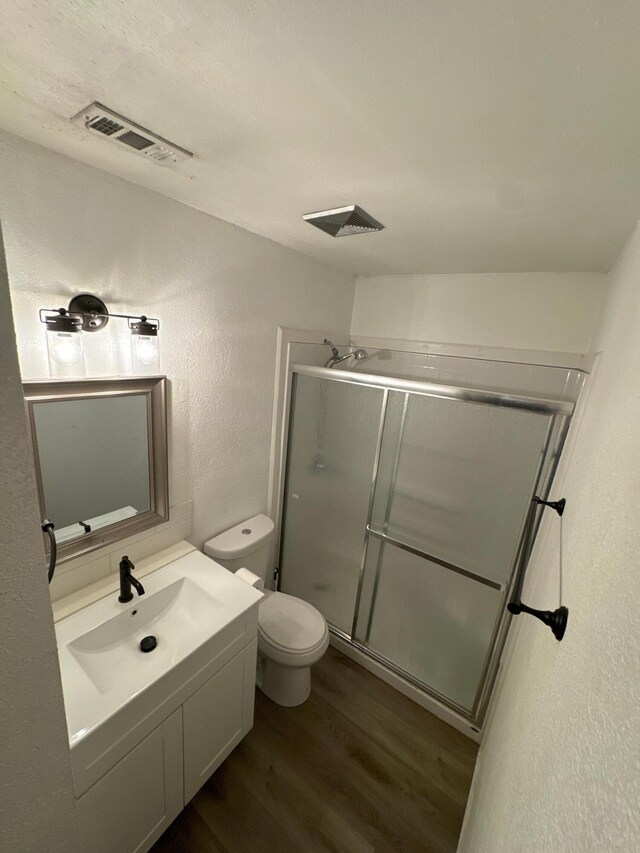 full bathroom with a textured wall, toilet, wood finished floors, vanity, and a stall shower