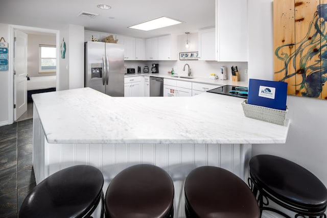 kitchen featuring visible vents, appliances with stainless steel finishes, white cabinetry, a sink, and a peninsula