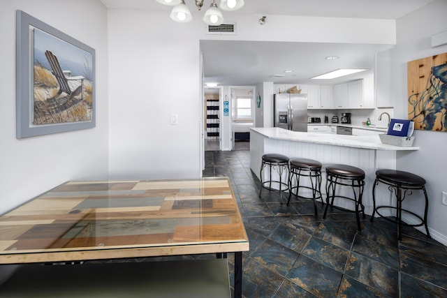 kitchen featuring visible vents, white cabinets, a sink, stainless steel fridge, and a peninsula